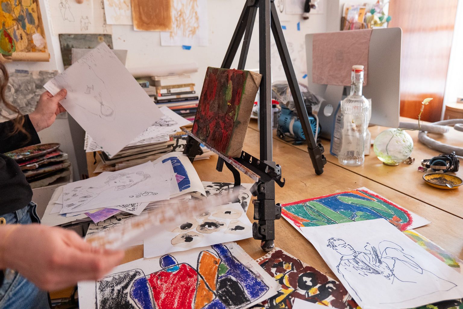 Artistic workspace with drawings on a table and an easel.